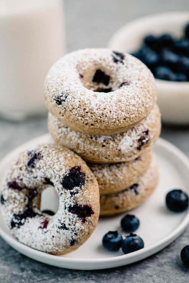 Baked Blueberry Donuts topped with powdered sugar, stacked on a white plate