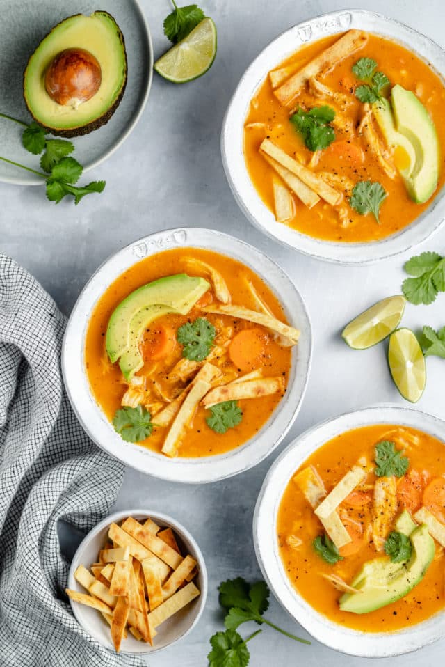 bowls of healthy tortilla soup served with tortilla strips, lime wedges and avocado slices