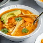 healthy chicken tortilla soup served with tortilla strips and slices of avocado