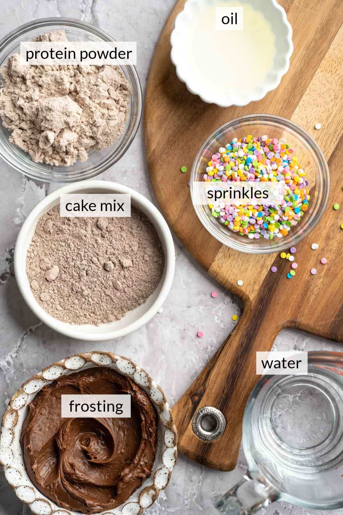 Small bowls with cake mix, protein powder, sprinkles, frosting and water.