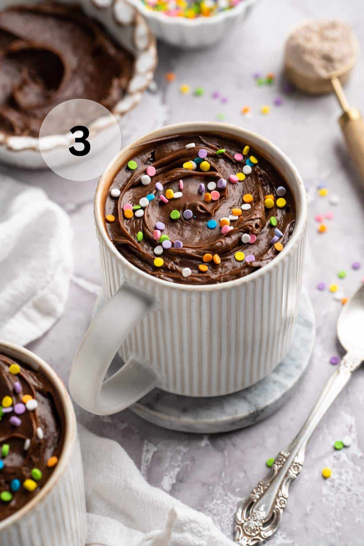 Mug cake topped with chocolate frosting and sprinkles.