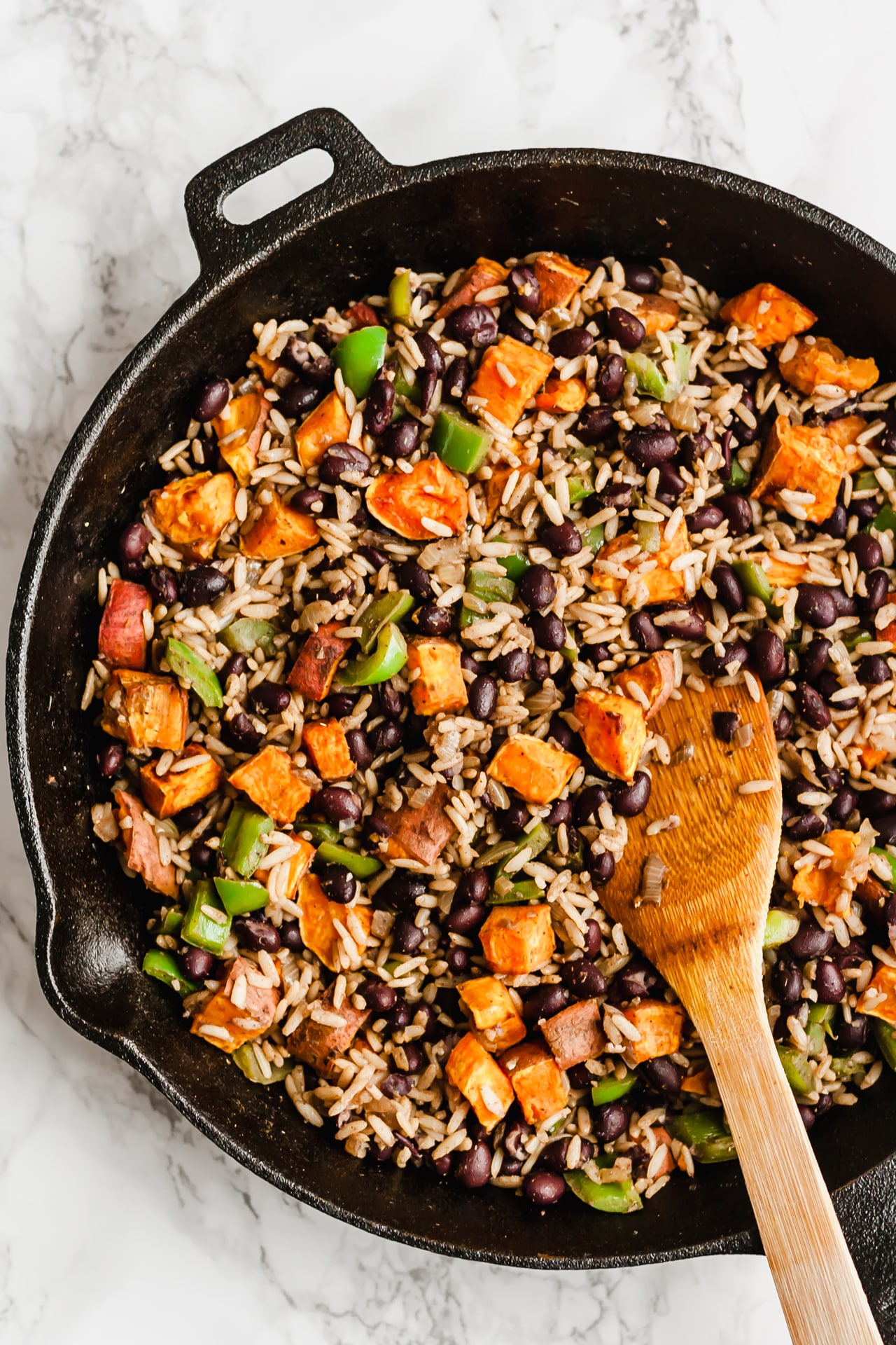 Stirring together cubed sweet potato with black beans, rice and veggies in a pan.