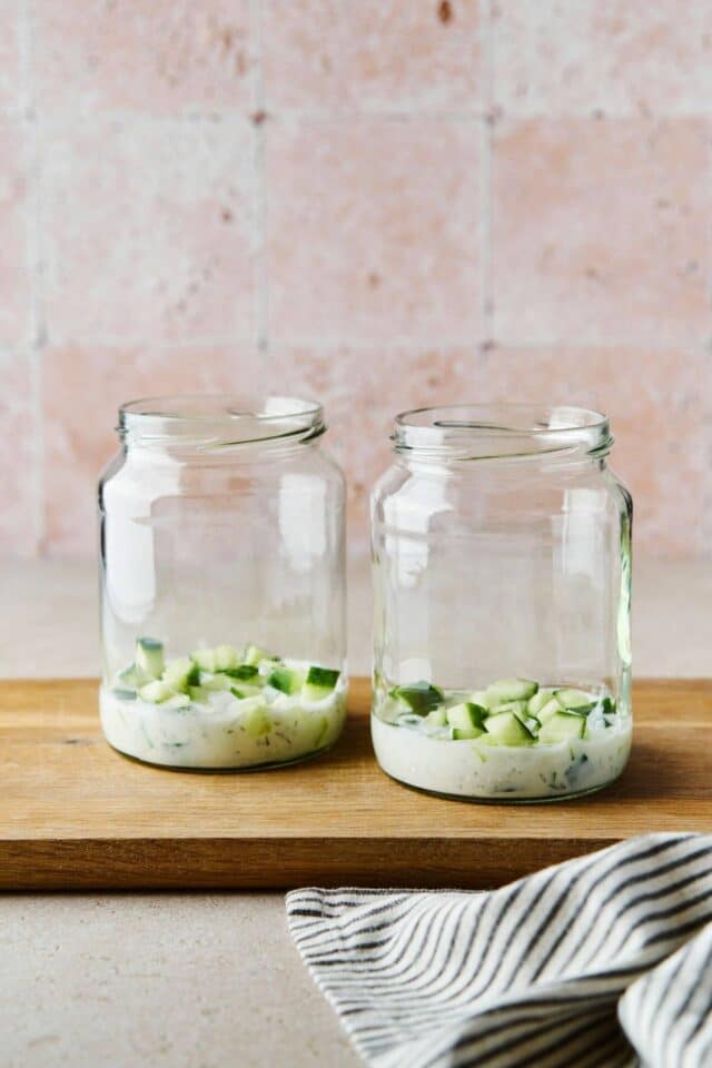 Dressing at the bottom of mason jars with cucumbers.