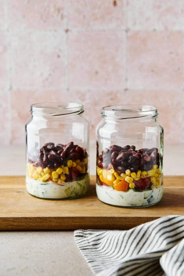 Dressing, tomatoes, corn and black beans layered in a mason jar.