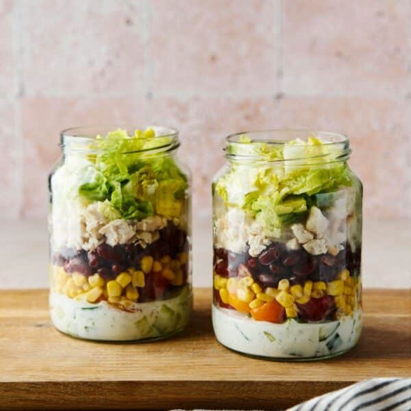 Layered salad in a jar with a creamy white dressing, corn, black beans, chicken and lettuce.