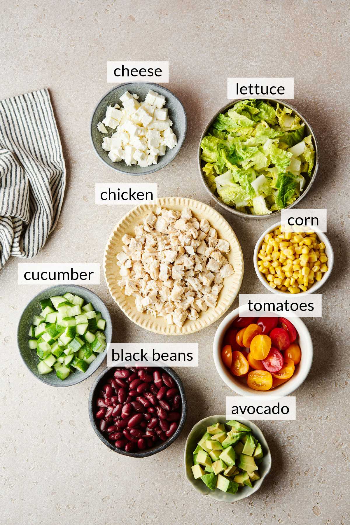 Bowls filled with chicken, black beans, corn, lettuce, cheese and cucumber.