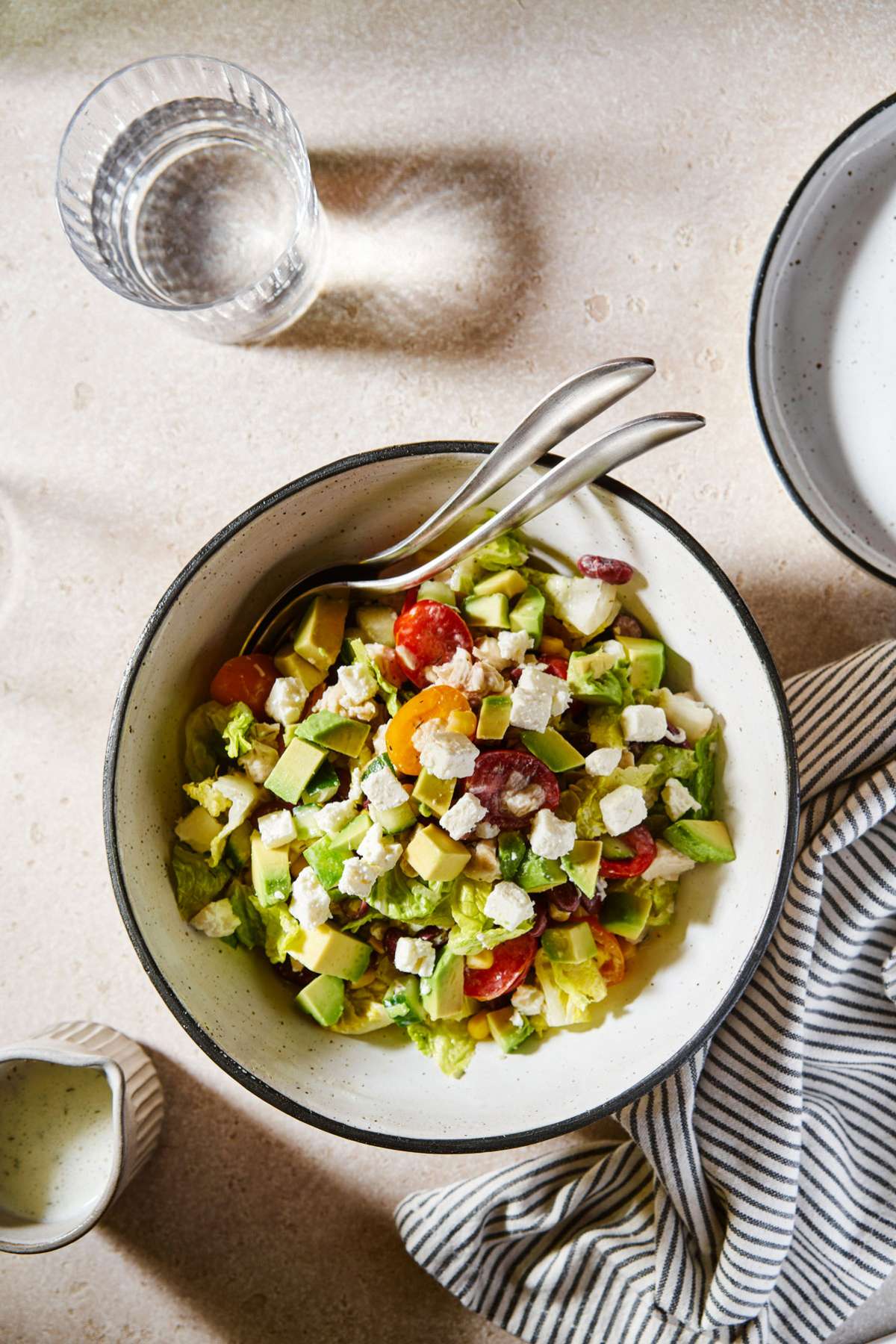 Lettuce topped with tomatoes, corn, black beans, avocado and crumbled cheese in a bowl.