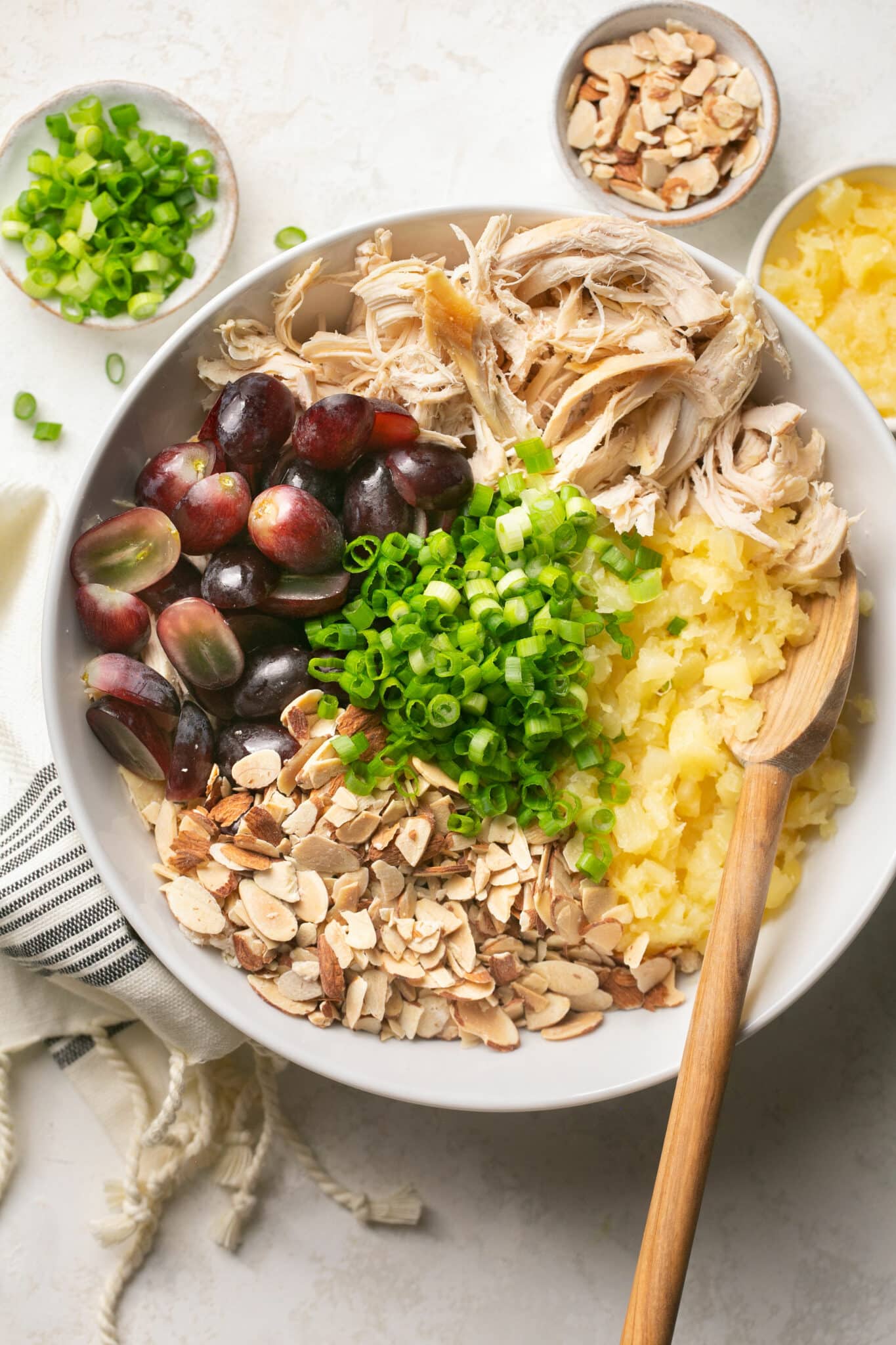 Shredded chicken, grapes, almonds and pineapple added to a large white bowl.