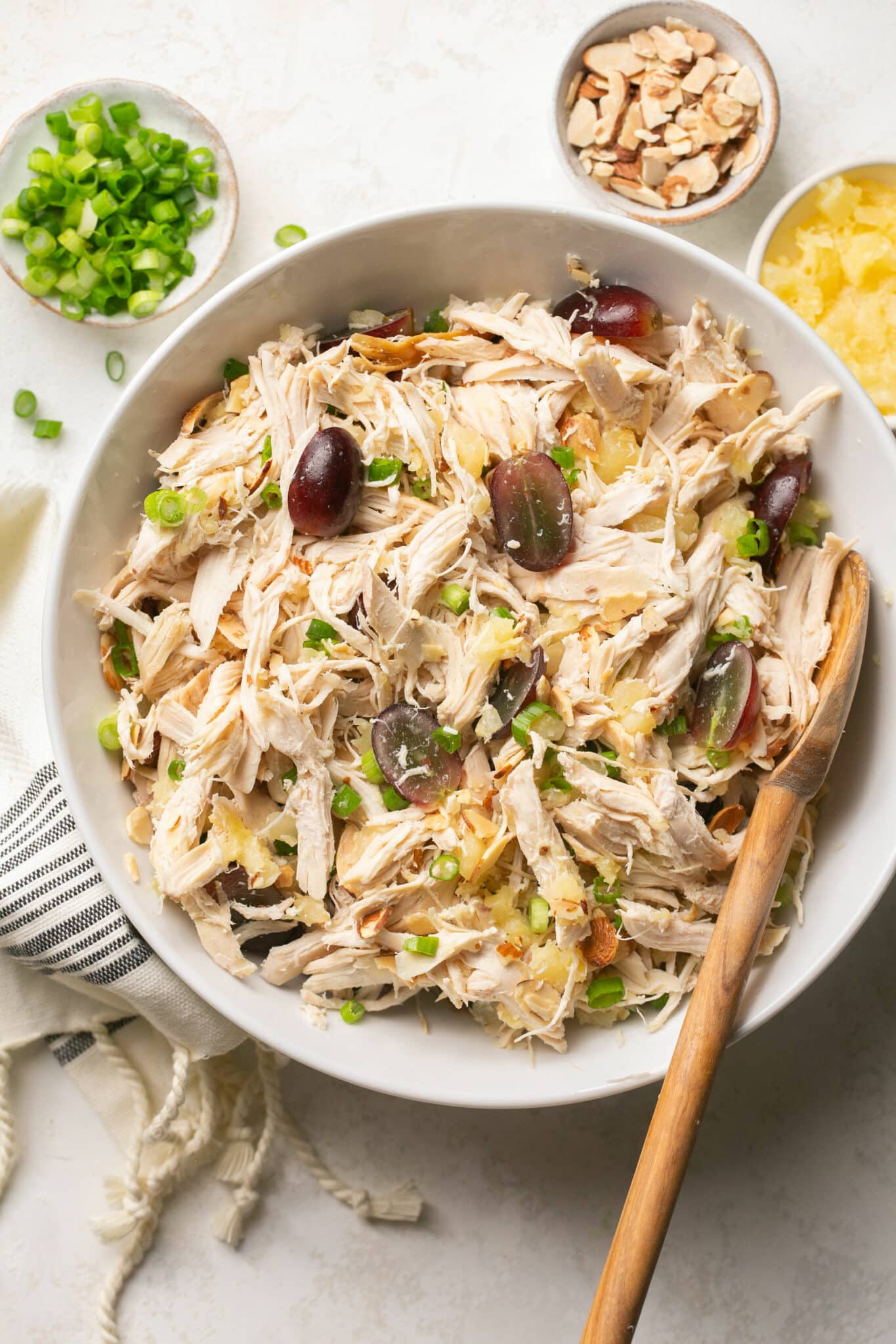 Mixing shredded chicken with grapes and green onions.