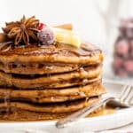 Stack of gingerbread pancakes topped with butter, syrup and sugared cranberries.