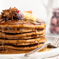 Stack of gingerbread pancakes topped with butter, syrup and sugared cranberries.