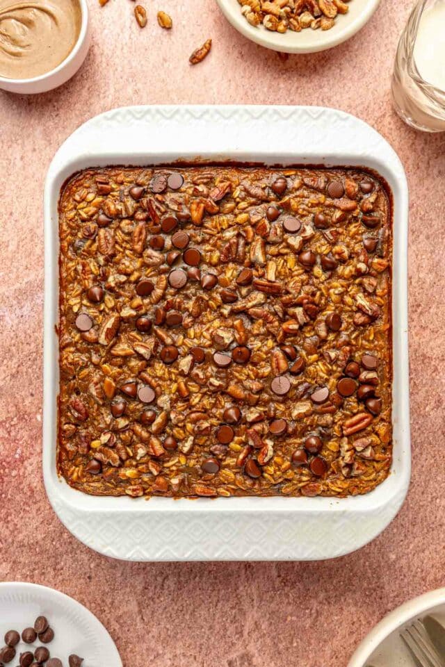 Baked oatmeal topped with pecans and chocolate chips in white dish.