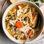 Chicken noodle soup with spoon in a white bowl and a lemon slice on the side