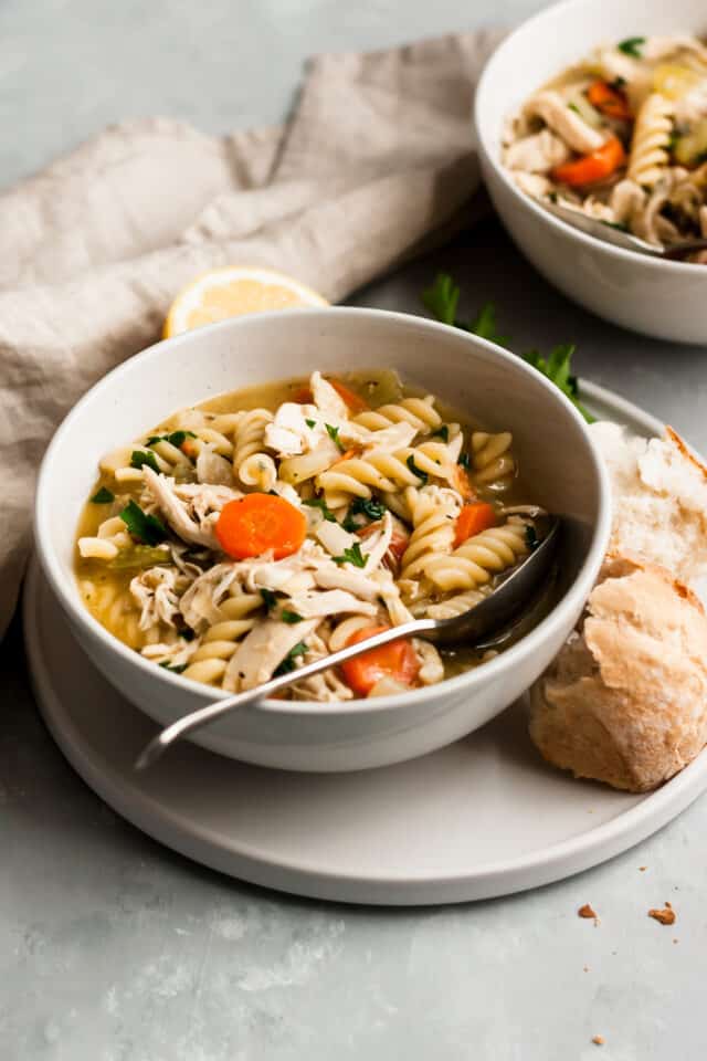 chicken noodle soup in a white bowl on a white plate served with bread