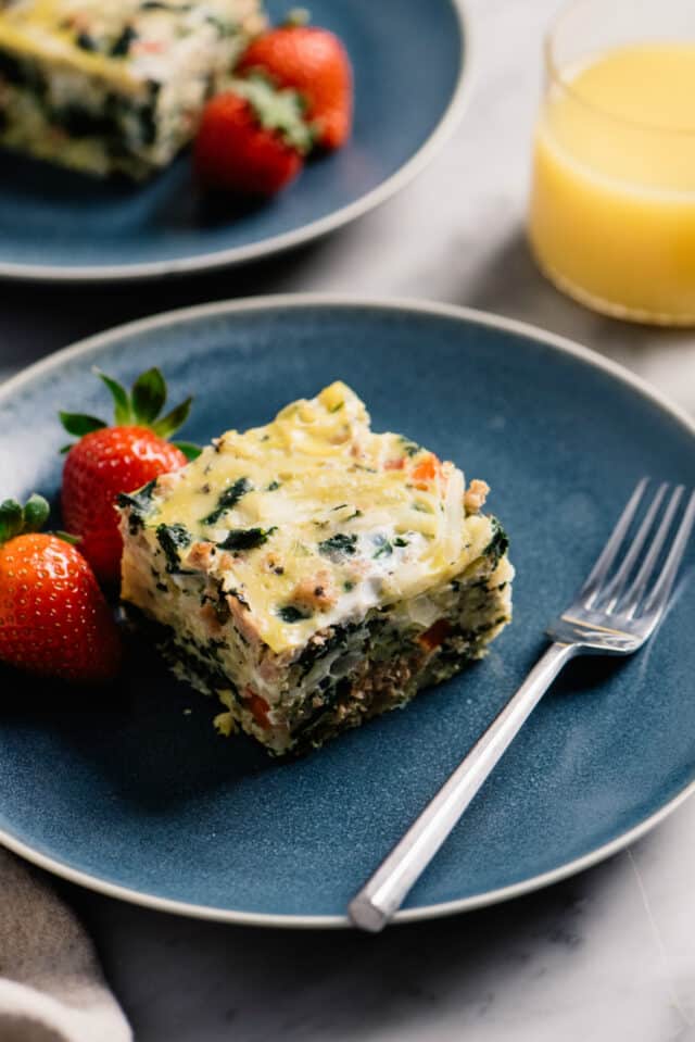 serving of egg casserole on a blue plate with strawberries and a fork