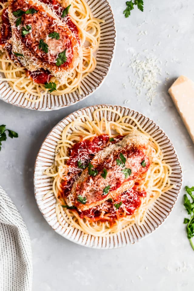 baked chicken parmesan served over pasta and garnished with fresh parsley 