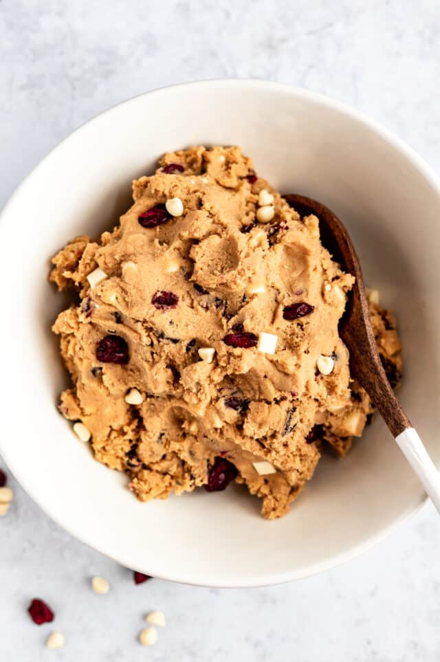 cookie batter that has white chocolate chips and dried cranberries in a white mixing bowl 