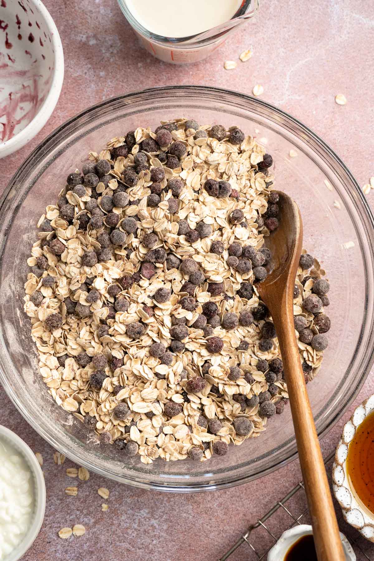 Using a wooden spoon to stir oats with blueberries in a large bowl.