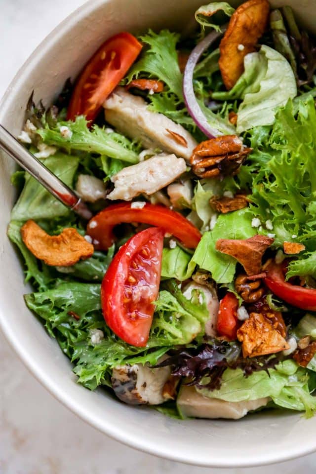 green salad topped with fresh tomatoes, grilled chicken, crisp apple and pecans