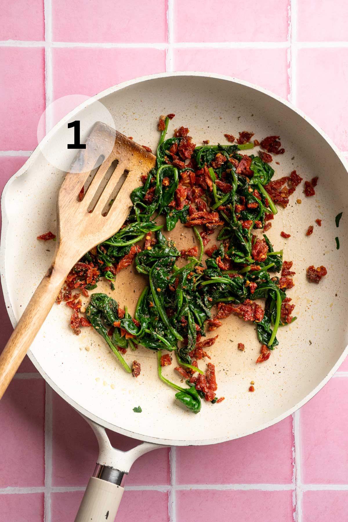Cooking spinach with sun-dried tomatoes in a large skillet.