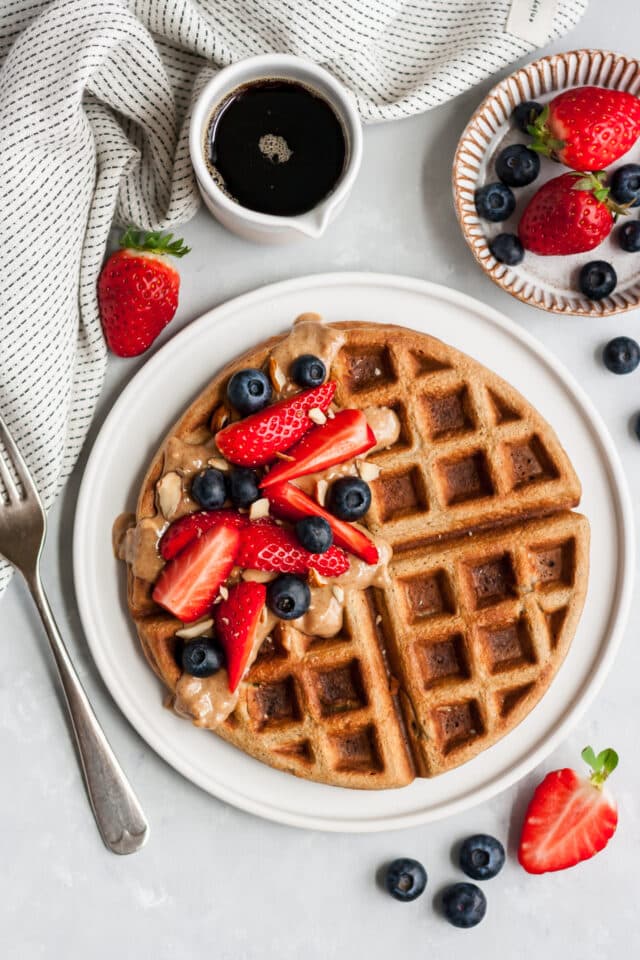 waffle on a white plate topped with fresh berries and almond butter