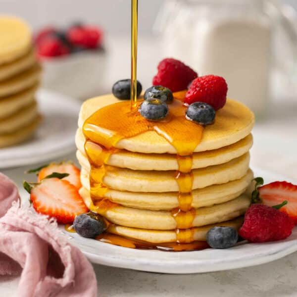 A stack of fluffy gluten free pancakes drizzled with maple syrup.