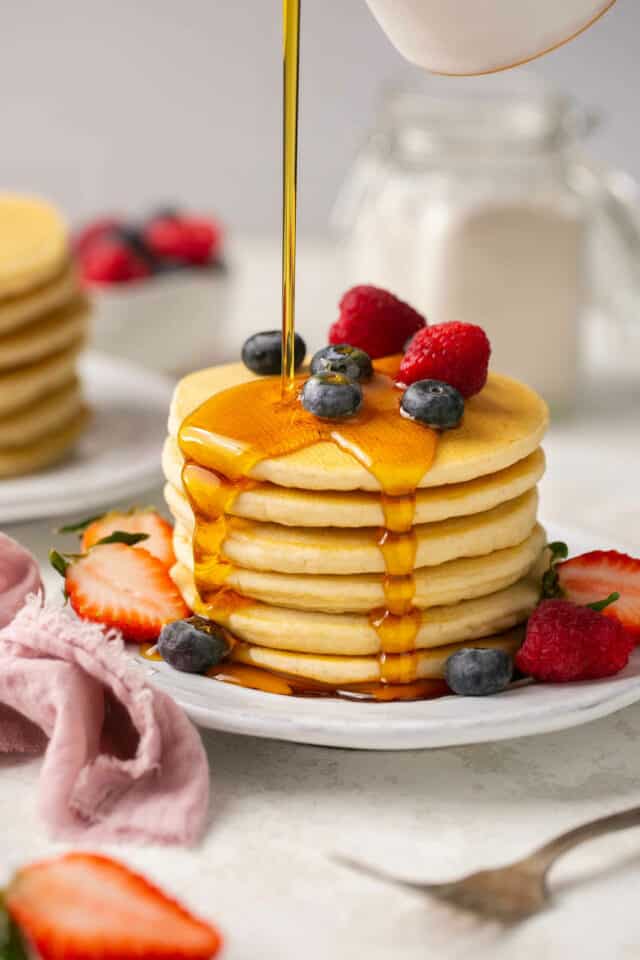 A stack of fluffy gluten free pancakes drizzled with maple syrup.
