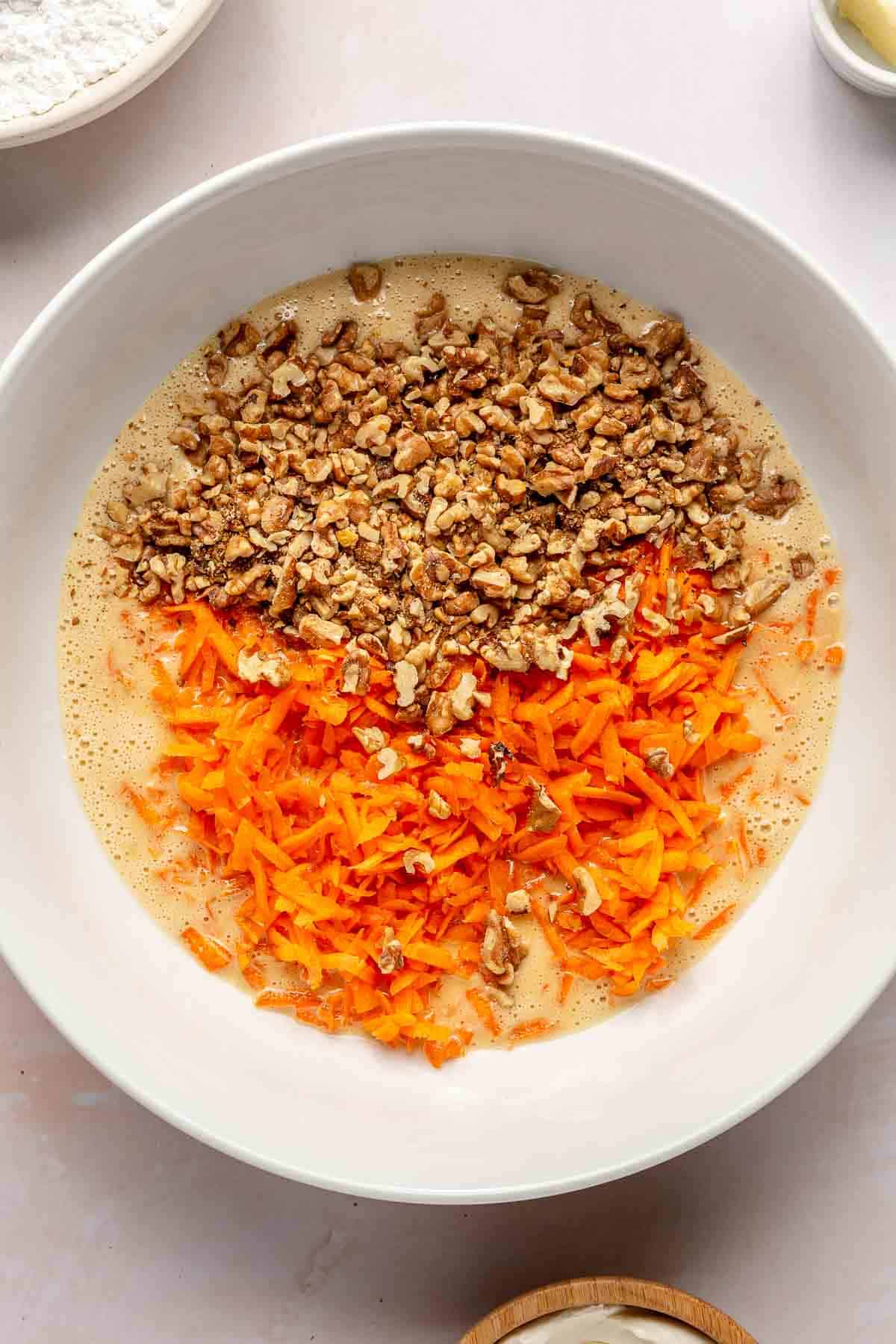 Carrots and walnut in a bowl with egg mixture.