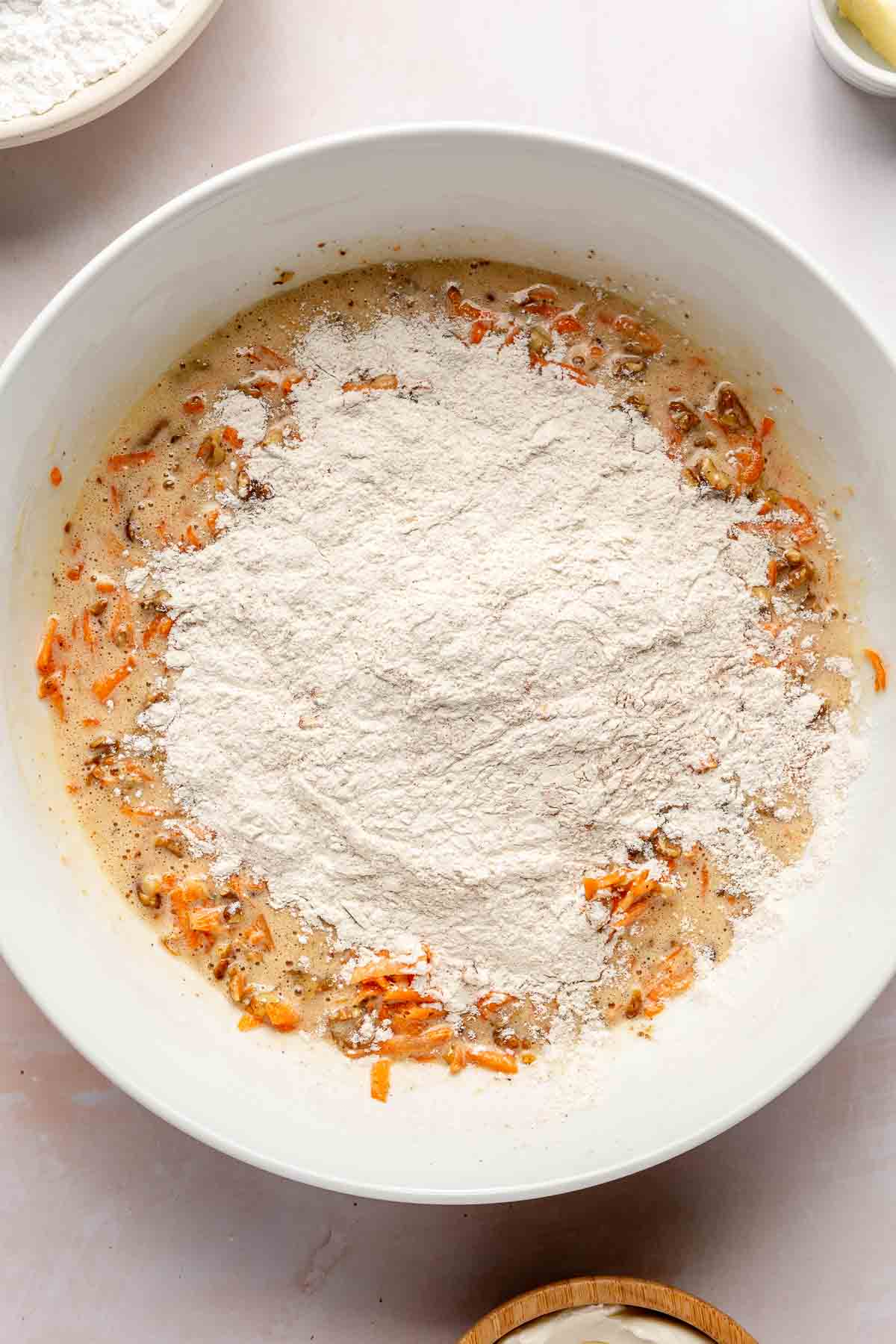 Adding flour to wet ingredients in a large white bowl.