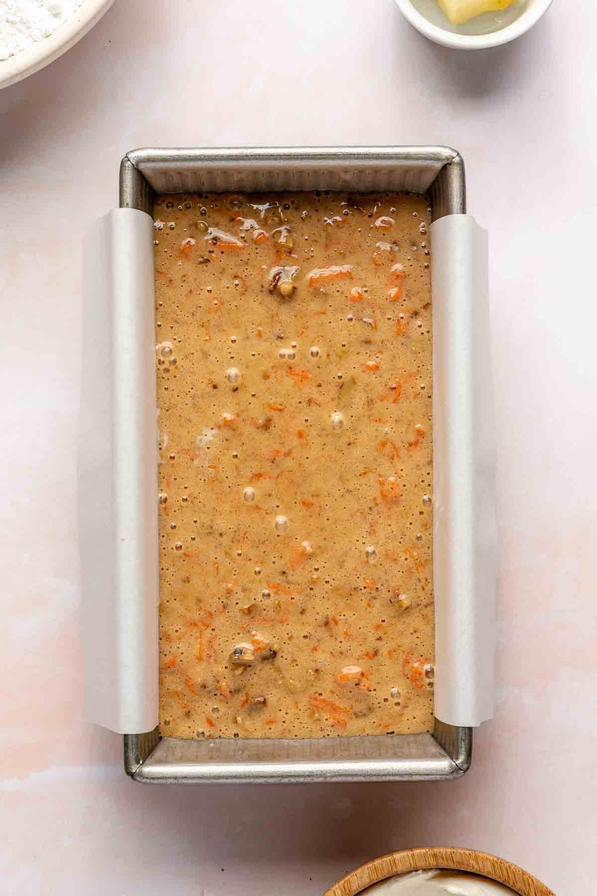 Carrot cake batter in a loaf pan lined with parchment paper.