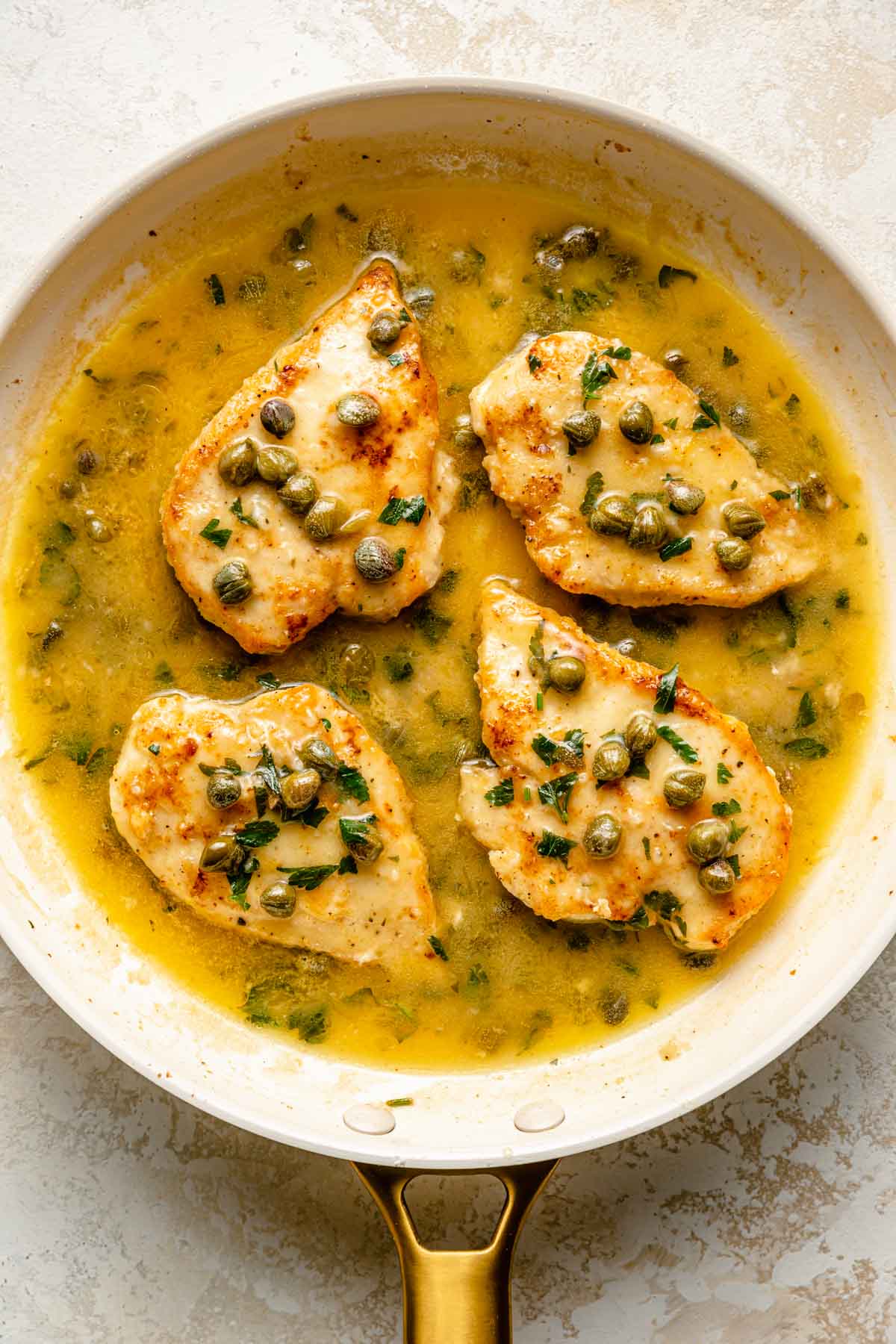 Chicken cutlets in a lemon sauce cooking in a skillet.