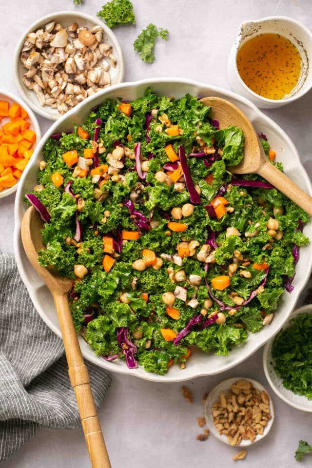 Kale salad in a serving bowl with large salad tongs.