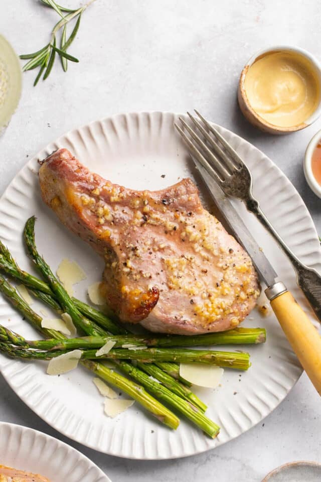 Pork chop on a white plate with roasted asparagus. 