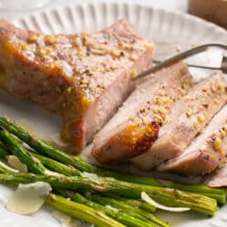 A sliced pork chop on a plate with asparagus.