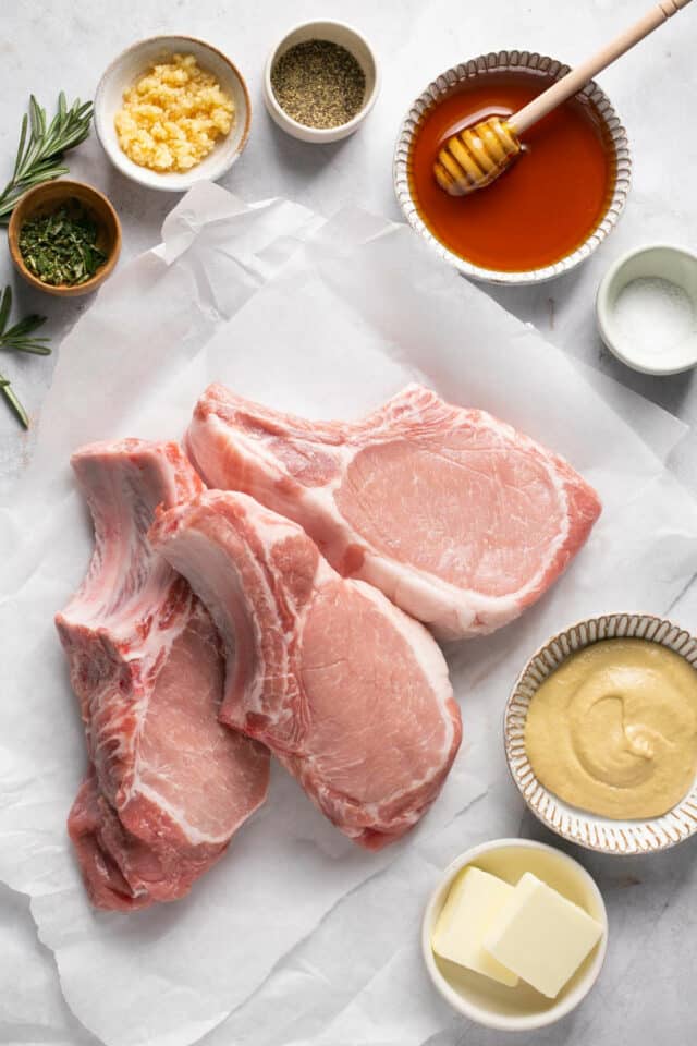 Raw pork chops on parchment paper with other ingredients in small bowls.