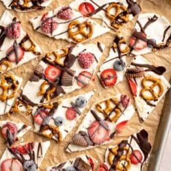 Frozen yogurt bark topped with berries, pretzels and chocolate on a sheet pan.