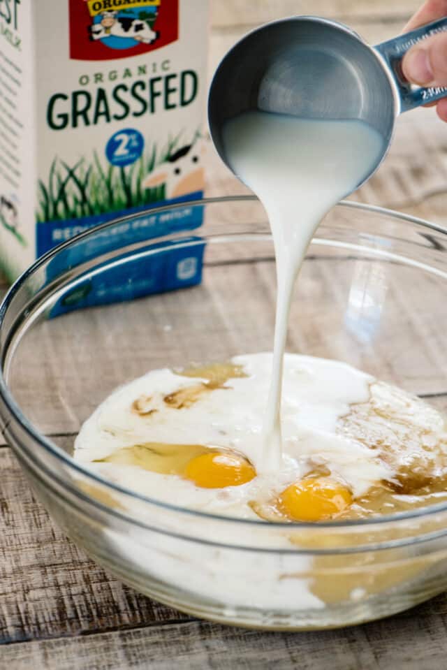 pouring milk into glass mixing bowl with eggs and other muffin ingredients 