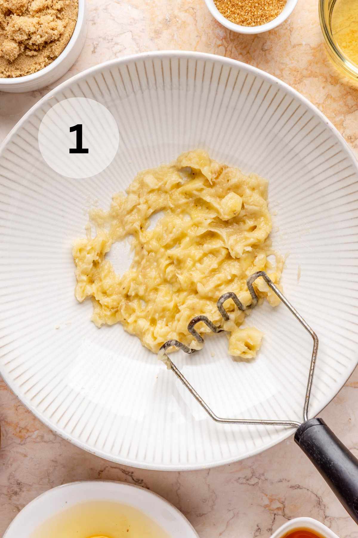 Mashing a banana in a white bowl with a potato masher.