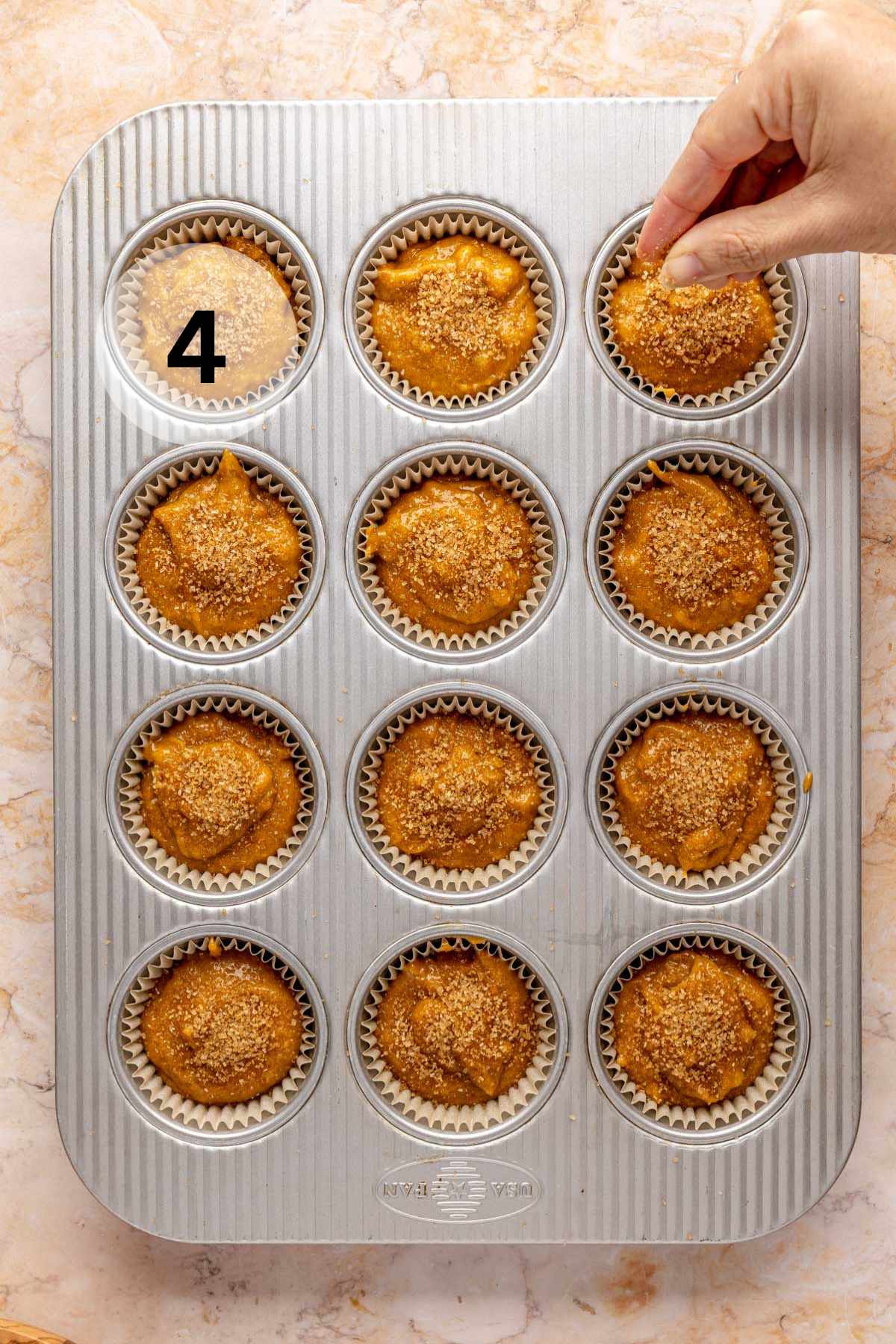 Sprinkling sugar over pumpkin muffin batter in a muffin pan.