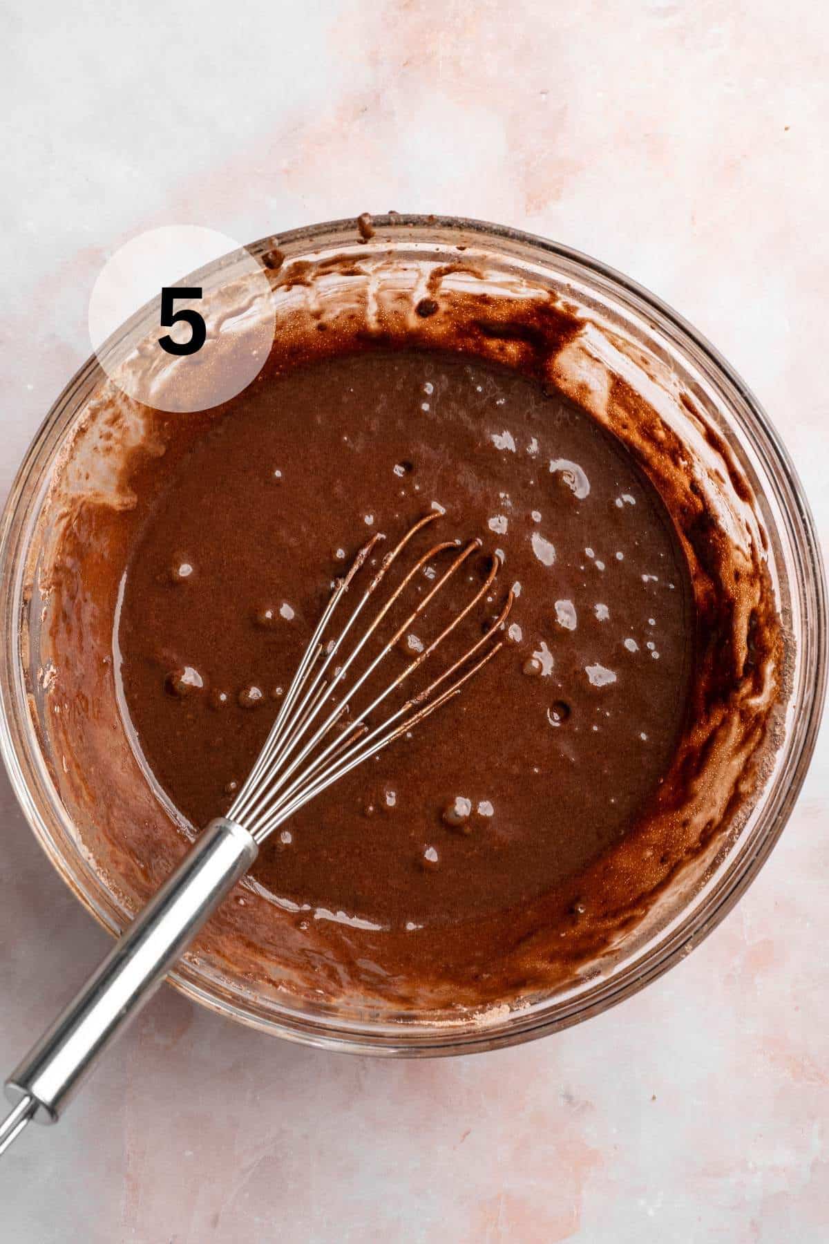 Whisking chocolate cupcake batter in a large glass bowl.