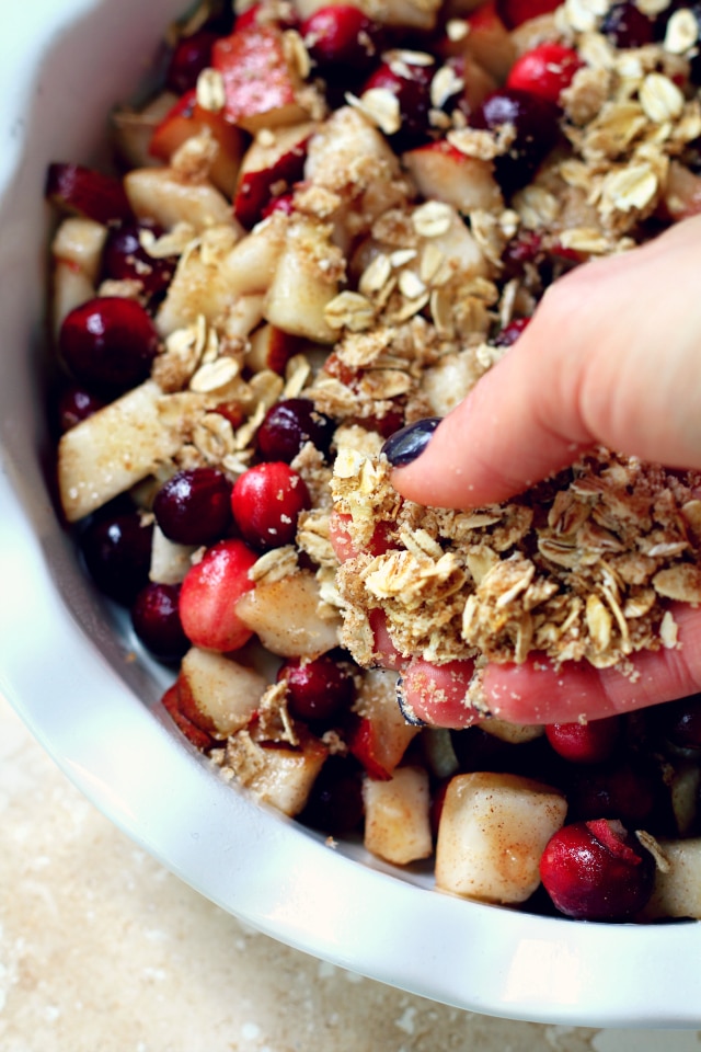 woman's hand spreading oat crumble crust over chopped pear and cranberries 