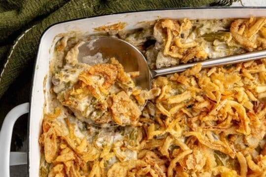 Serving green bean casserole with a large silver serving spoon.
