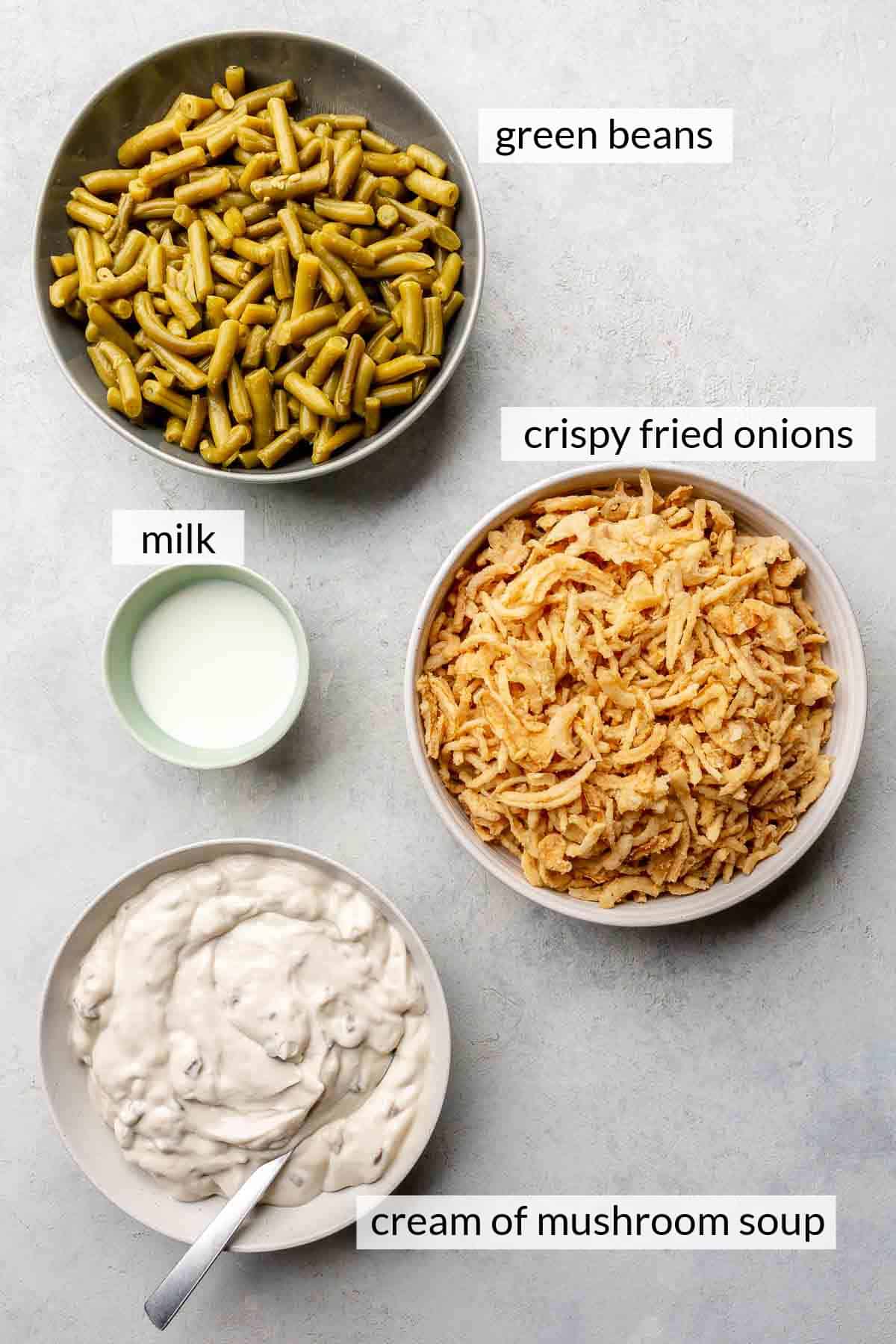 Green beans, cream of mushroom soup, milk and crispy fried onions divided into small bowls.