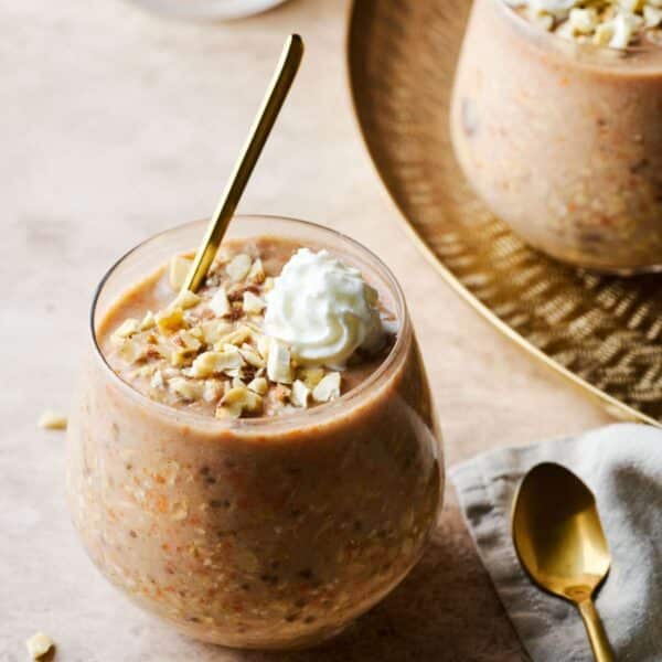 Carrot cake overnight oats in a small glass topped with whipped cream.