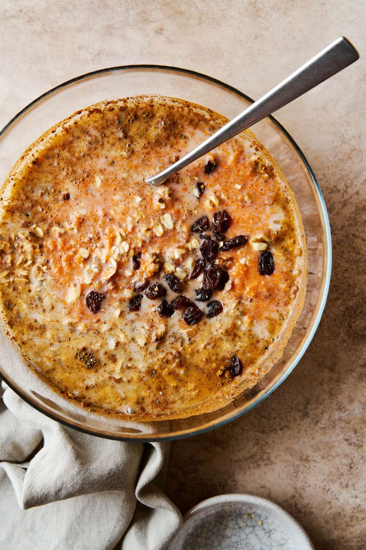 Stirring in grated carrots and raisins to oatmeal mixture in a large bowl.