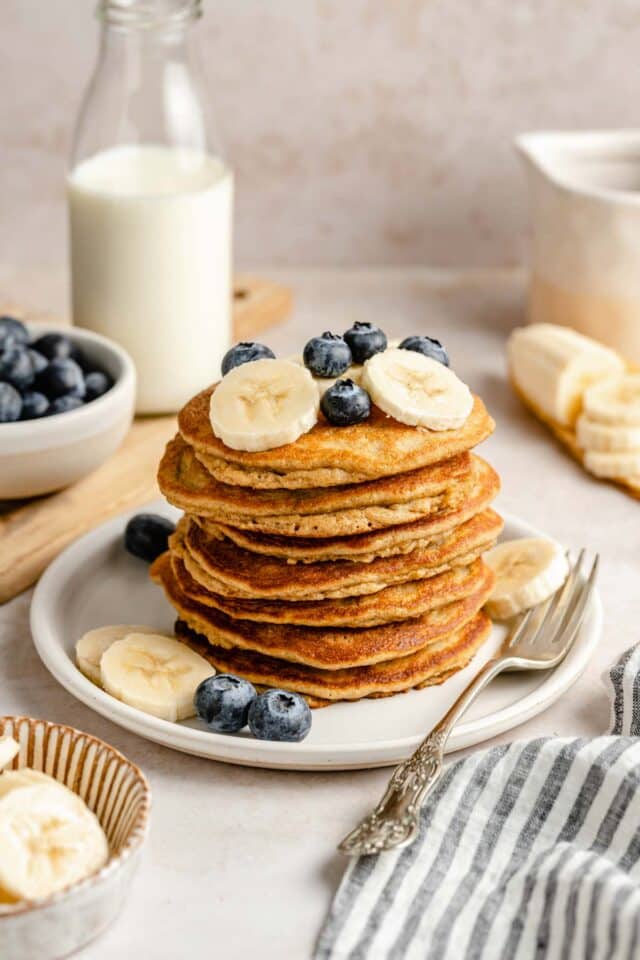 Pancakes on a white plate topped with banana slices and blueberries.