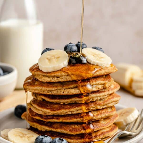 A stack of coconut flour pancakes topped with fruit and drizzled with maple syrup.