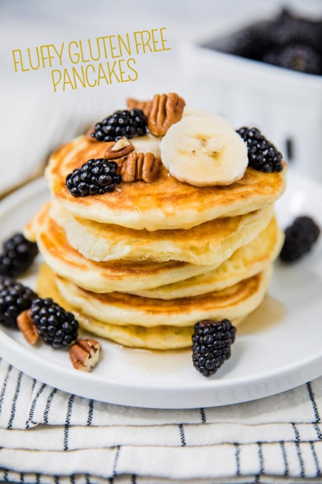 pancakes on a white plate topped with blackberries and pecans