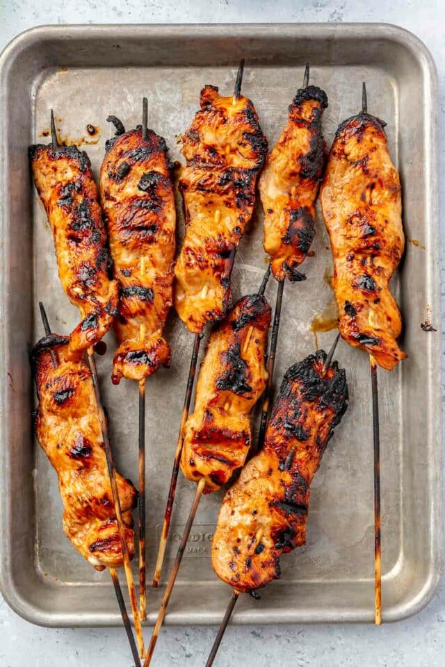 Grilled chicken on wooden skewers on a pan.