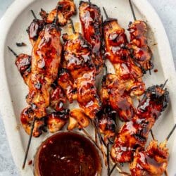 Glazed chicken skewers on a serving plate with BBQ sauce.